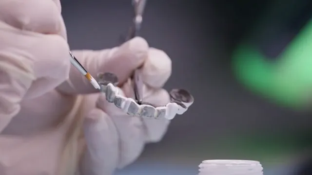 Gloved hands use a fine brush on a dental restoration.