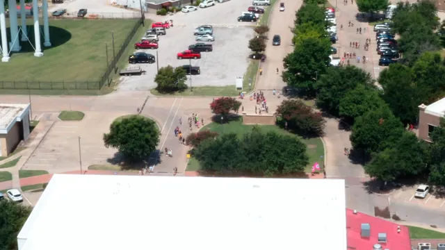 Aerial view of a campus with a water tower, trees, and a white-roofed building.