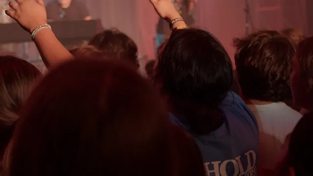 People seen from behind with raised arms in warm red light.