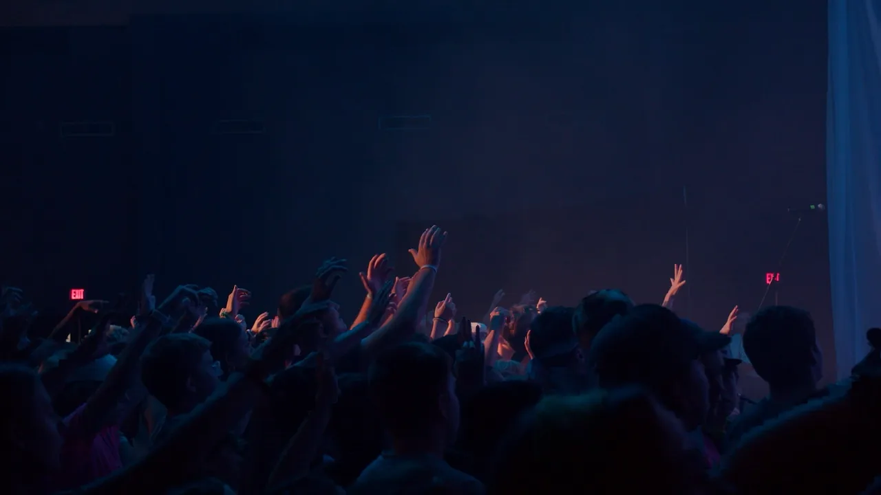 Silhouetted hands raised in a dark hall under stage light.