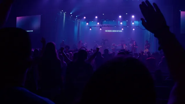 Silhouetted hands raised toward a blue-lit stage with a band.