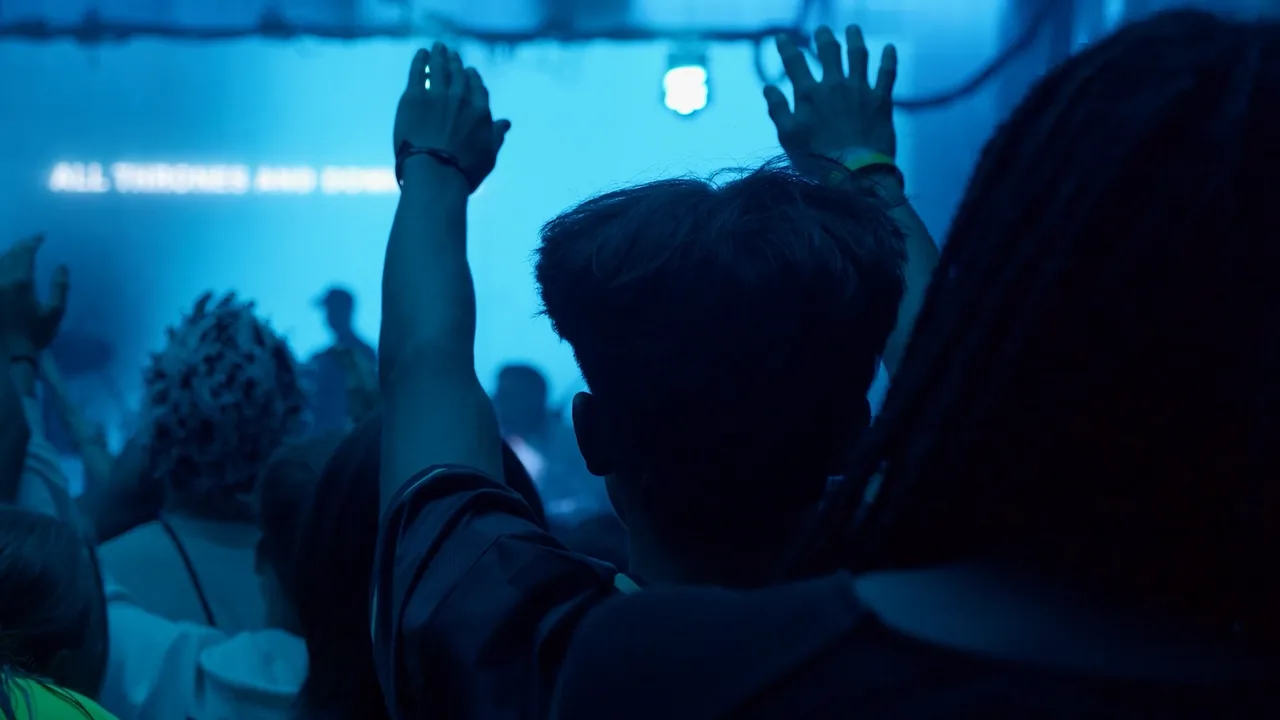 A person seen from behind raises a hand toward a blue-lit stage screen.