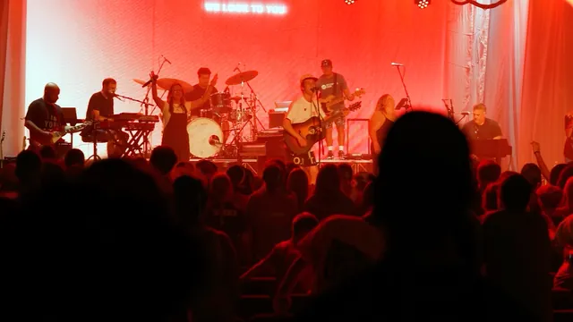 A band performs on a red-lit stage above a silhouetted crowd.