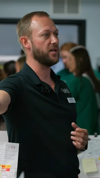 A lab staff member in a black polo points while explaining something to a group.