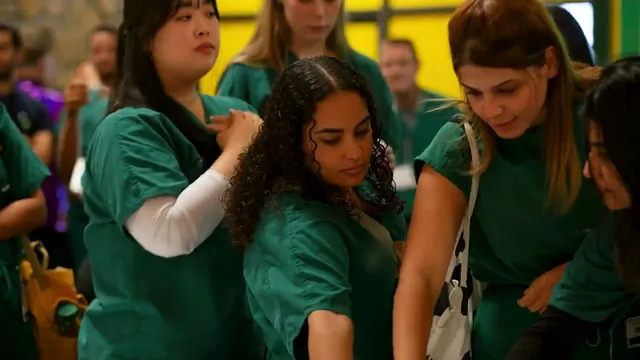 Students in green scrubs lean in to look at something together.