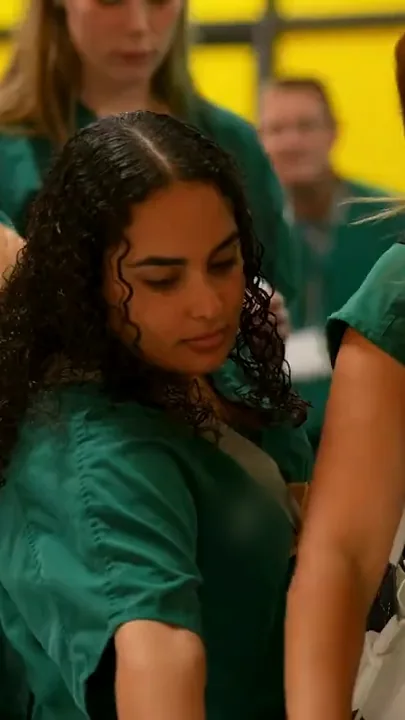 Dental students in green scrubs lean in to look at something together.